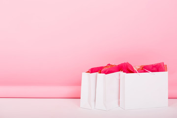 Three big white paper bags from gift shop standing on the floor on cute pink background. Photo of...