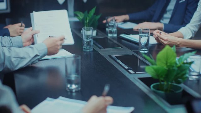 In the Corporate Meeting Room Close-up on the Hands of Businesspeople, Signing Contracts, Using Smartphones and Digital Tablet Computers, Gesticulating. People Sitting at Conference Table