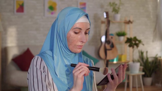 Muslim woman in a hijab with a burn scar on her face doing makeup