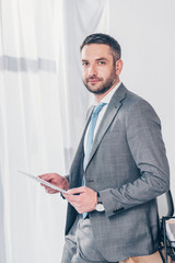 handsome businessman in suit holding newspaper and looking at camera