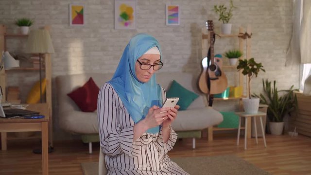 Young muslim woman in hijab with a scar from a burn on her face uses a smartphone