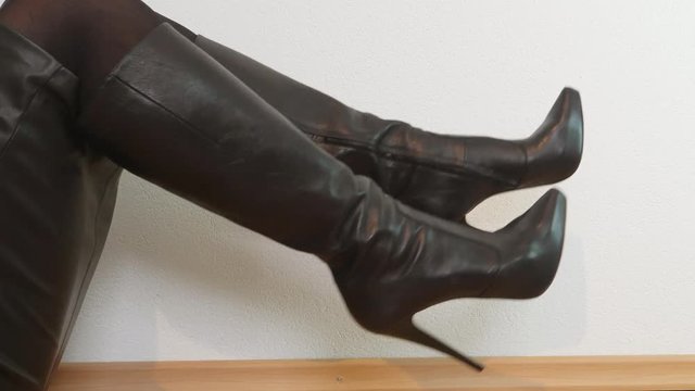 Woman sitting on the ground wearing high black platform boots moves both alternately up and down