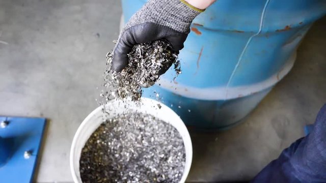 Moving shot of gloved hand dropping processed metal scrap into a bucket