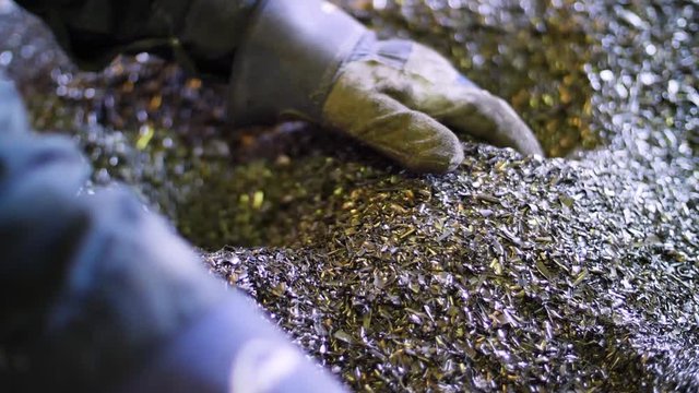 Pair of gloved hands scoop up metal pieces at metal recycling plant