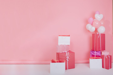 Photo of big bright presents and white party balloons for birthday standing on the floor. Colorful gift boxes with cute ribbons for christmas or st. valentines day isolated on rose-colored background
