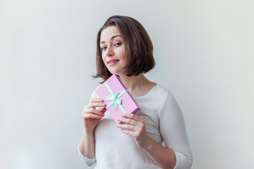 Young positive woman holding small pink gift box isolated on white background. Preparation for holiday. Girl looking happy and excited. Christmas birthday valentine celebration present concept