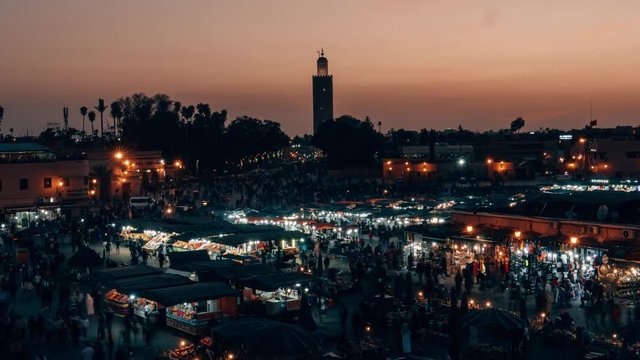 Timelapse stationary above a crowded marketplace Djemaa el Fna in Marrakech Morocco crowded with people buying and selling food and items at sunset turning to night