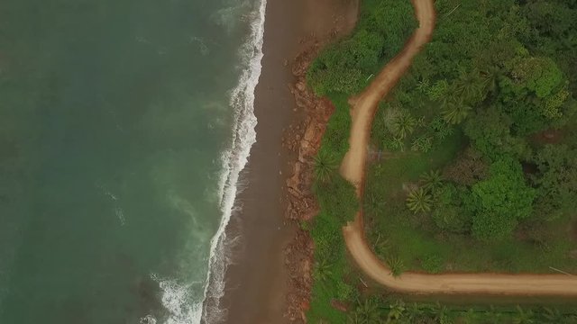Aerial view of interesting dirt road between small ocean waves and central american jungle