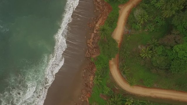 Aerial view of interesting dirt road between big ocean waves and central american jungle