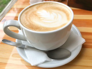 A large white cup of cappuccino with milk standing on a wooden table. Coffee mood. The concept of a break, pause. Delicious aromatic hot drink for relaxation. Close-up, yellow toning, warm atmosphere.