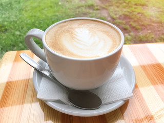 A large white cup of cappuccino with milk standing on a wooden table. Coffee mood. The concept of a break, pause. Delicious aromatic hot drink for relaxation. Close-up, yellow toning, warm atmosphere.