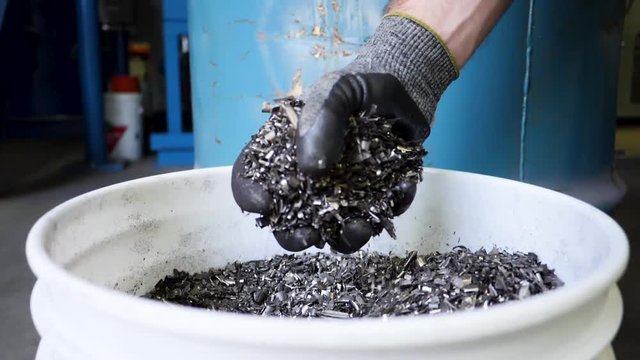 A gloved hand grabs metal turnings from a bucket in slow motion
