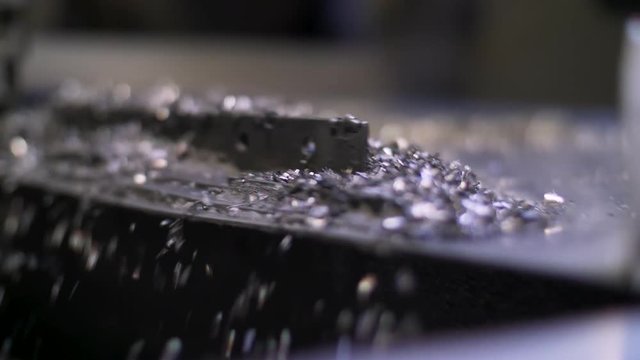 Close up of metal filings fall from a vibrating ramp into a large cardboard box