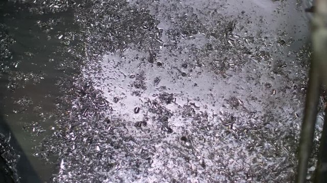 Tiny metal pieces vibrate down a water ramp at recycling factory