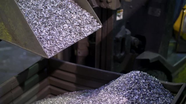 Hydraulic bucket pouring metal cobbles into larger bucket
