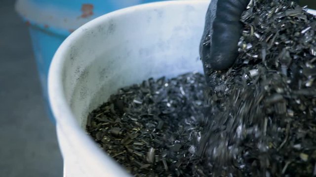 Gloved hand scoops metal turnings from white bucket