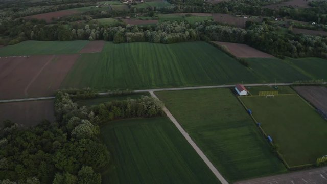 Drone footage in Bosnia and Herzegovina, Brcko district. Forwarding the drone and curving the camera and capturing beautiful football field, flat land with straight road. Green forest.