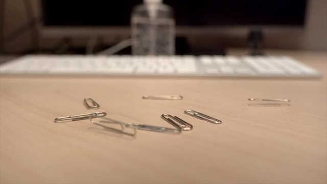 A hand full of paper clips slowly dropping onto an office desk in super slow motion a little bit at a time.