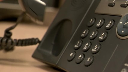 A close up of a desk office phone while a hand pushes buttons, removes the receiver and places it back on the base in slow motion.
