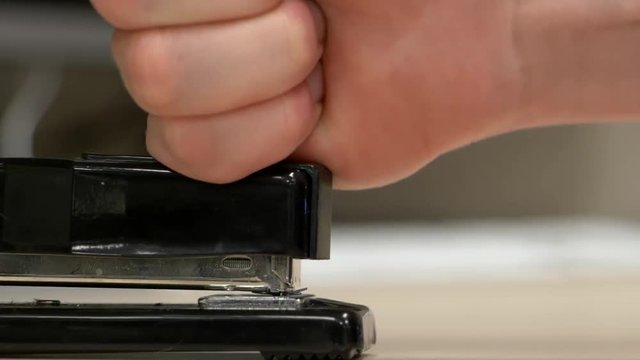 A profile view hand hitting a black stapler with no paper in it a bunch of times knocking staples out.