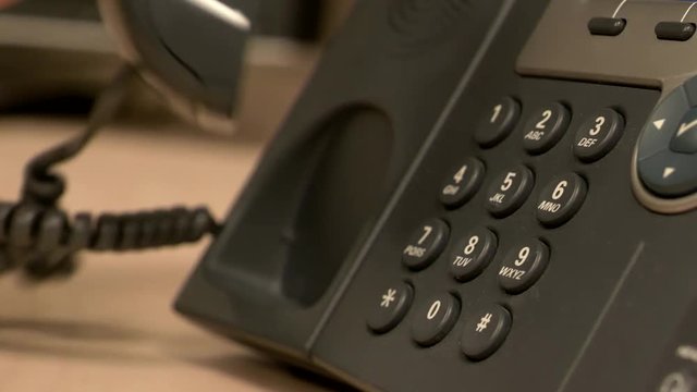 A close up of a desk office phone while a hand pushes buttons, removes the receiver and places it back on the base in slow motion.