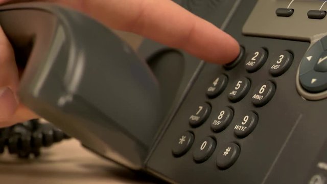 A close up of a desk office phone while a hand pushes buttons, removes the receiver and places it back on the base.