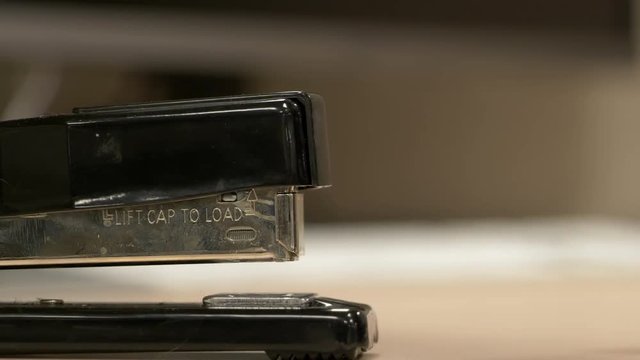 A close up from the side of a black stapler stapling pieces of paper together.