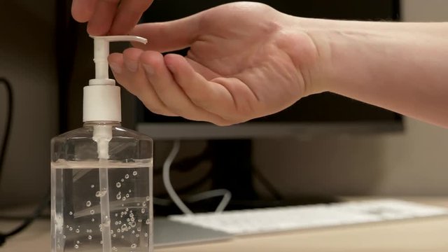 A pair of Caucasian hands pressing down on a hand sanitizer bottle dispensing a measure of liquid onto the hands as the hands then apply it in slow motion.