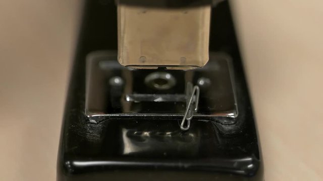 A hand hitting a black stapler with no paper in it a bunch of times knocking staples out. In slow motion.