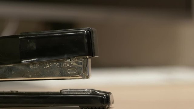 A close up from the side of a black stapler stapling pieces of paper together.