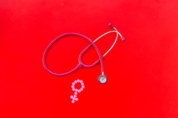 diagnostic and cure of gynaecological disease with stethoscope and female symbol on red background top view