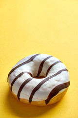 One single round donut with white ice glazing and stripes of dark brown chocolate on a yellow background with copy space. Vertical image