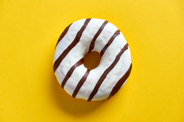 One single round donut with white ice glazing and stripes of dark brown chocolate on a yellow...