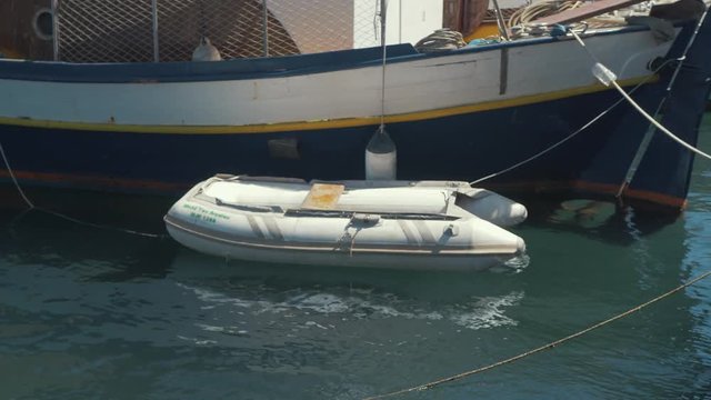 Small plastic dinghy tied to larger carvel built wooden sail boat in harbor