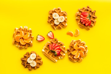 homemade Belgian waffles with fruit topings on yellow background top view