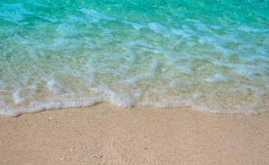Fototapeta na wymiar Soft wave of blue ocean on sandy beach Background with white wave bubbles.