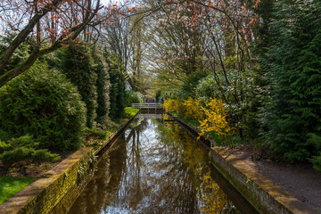 Diminishing perspective tranquil shady view of small canal, small white bridge and garden with bush, shrub, tulips flower and trees in spring season at Keukenhof gardens in Lisse, Netherlands.