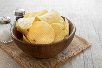 Potato chips in wood bowl  put on the mat with salt and pepper.back natural light food photo concept.