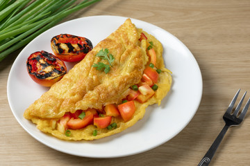 omelette tomato sliced and grill on white dish decorated with spring onion. wood table light side.