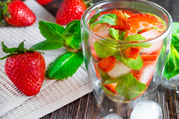 Summer drink of strawberries and mint with ice cubes on dark wooden table.
