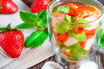 Fresh strawberry mojito or lemonade with mint and ice cubes on dark wooden table.