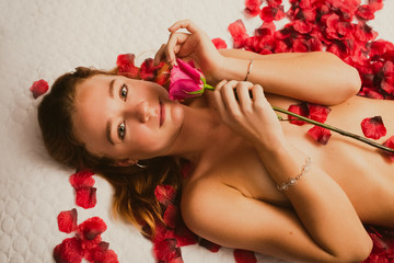 Redhead caucasian poses on bed covered in rose petals
