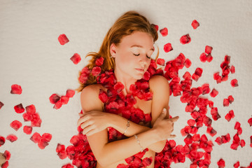 Obraz na płótnie Canvas Redhead caucasian poses on bed covered in rose petals