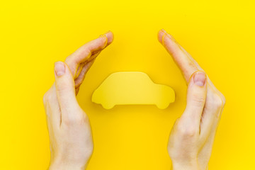 Car buying and insurance concept with car figure in hands on yellow background top view