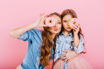 Attractive curly girl in denim shirt embracing little sister and funny posing with delicious donut...