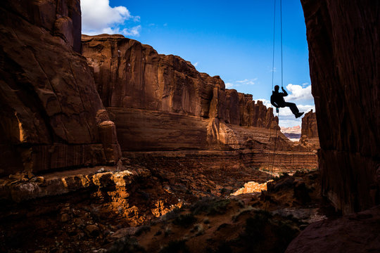 Entering a narrow canyon hanging in air, rappelling in Arches National Park, Utah.