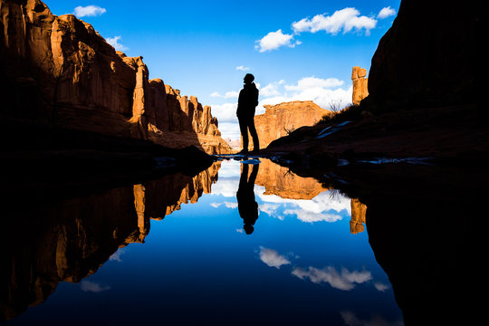 Reflection in calm lake in the desert of Southern Utah. Reflection of a man standing by the pond as well as red rock towers and canyon walls.