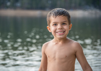 Smiling shirtless little boy swimming in mountain lake