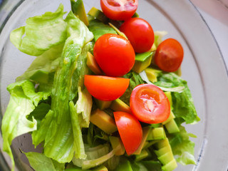 Hand is squeezing lime over vegetarian salad is made from avocado, tomatoes, cucumber and basil.