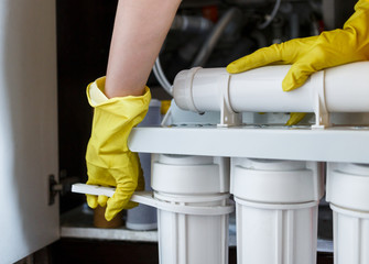 Plumber in yellow household gloves changes water filters. Repairman changing water filter...